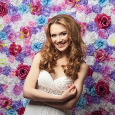 Beautiful woman smiling, wearing a wedding dress on a background of flowers. Emotion shyness