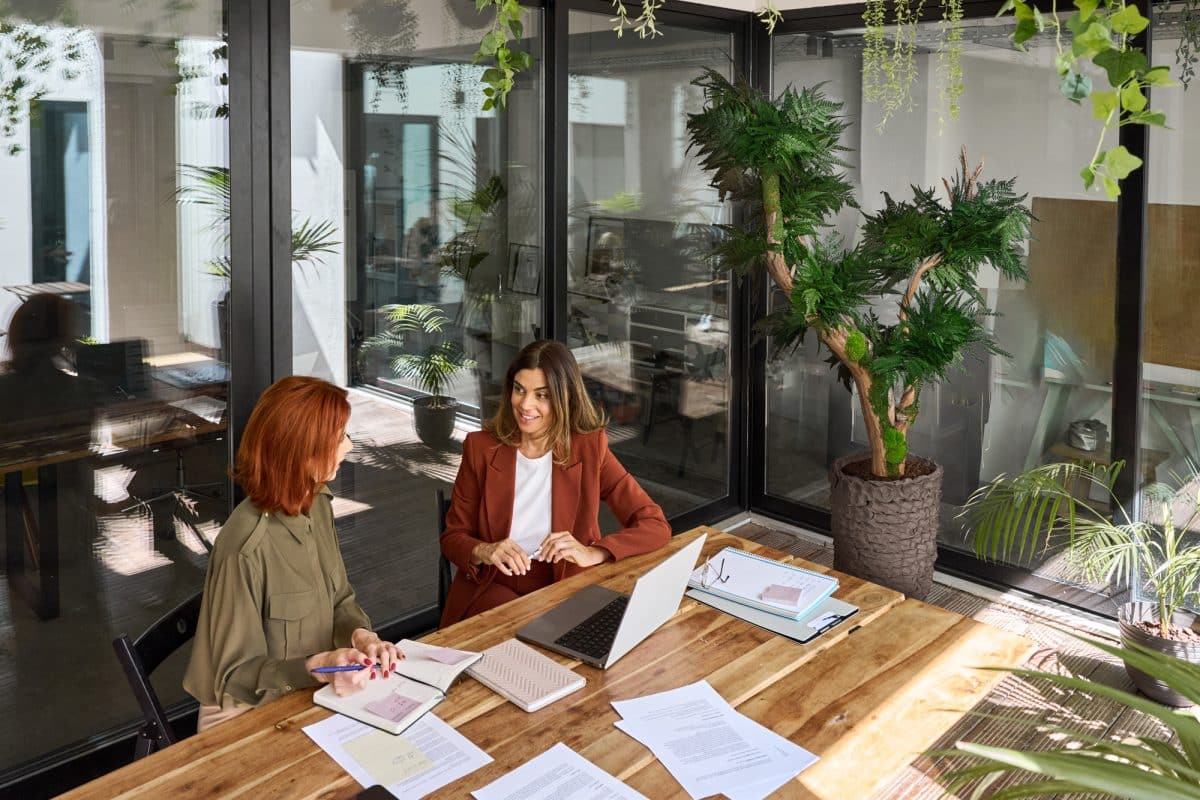 Two busy business women talking working at desk in green office. Top view.